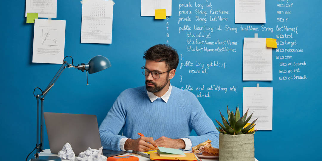 Man sitz am Schreibtisch und schaut auf einen Rechner vor einer blauen Wand - Content-Marketing